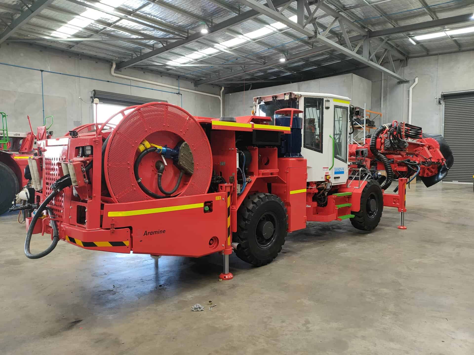 Stationary red underground mining jumbo drill rig in grey shed setting